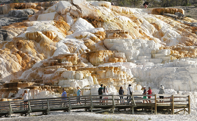 People are standing on a boardwalk in front of hot spring travertine terraces.