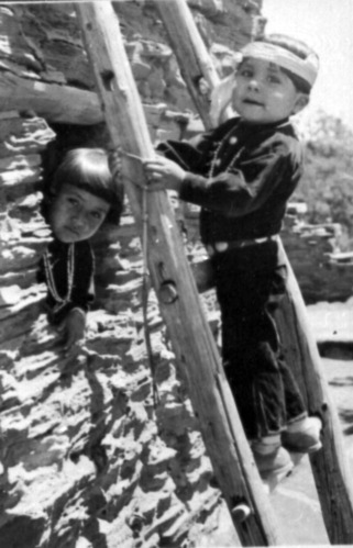 Black and white photograph of two young kids playing in/outside of Hopi House. La Verne Timeche is poking her head out a window, and Billy Timeche is on a ladder at her level. 
