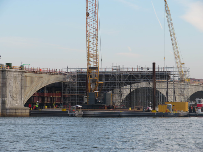 Scaffolding and a construction work place are set up on the water next to the bridge