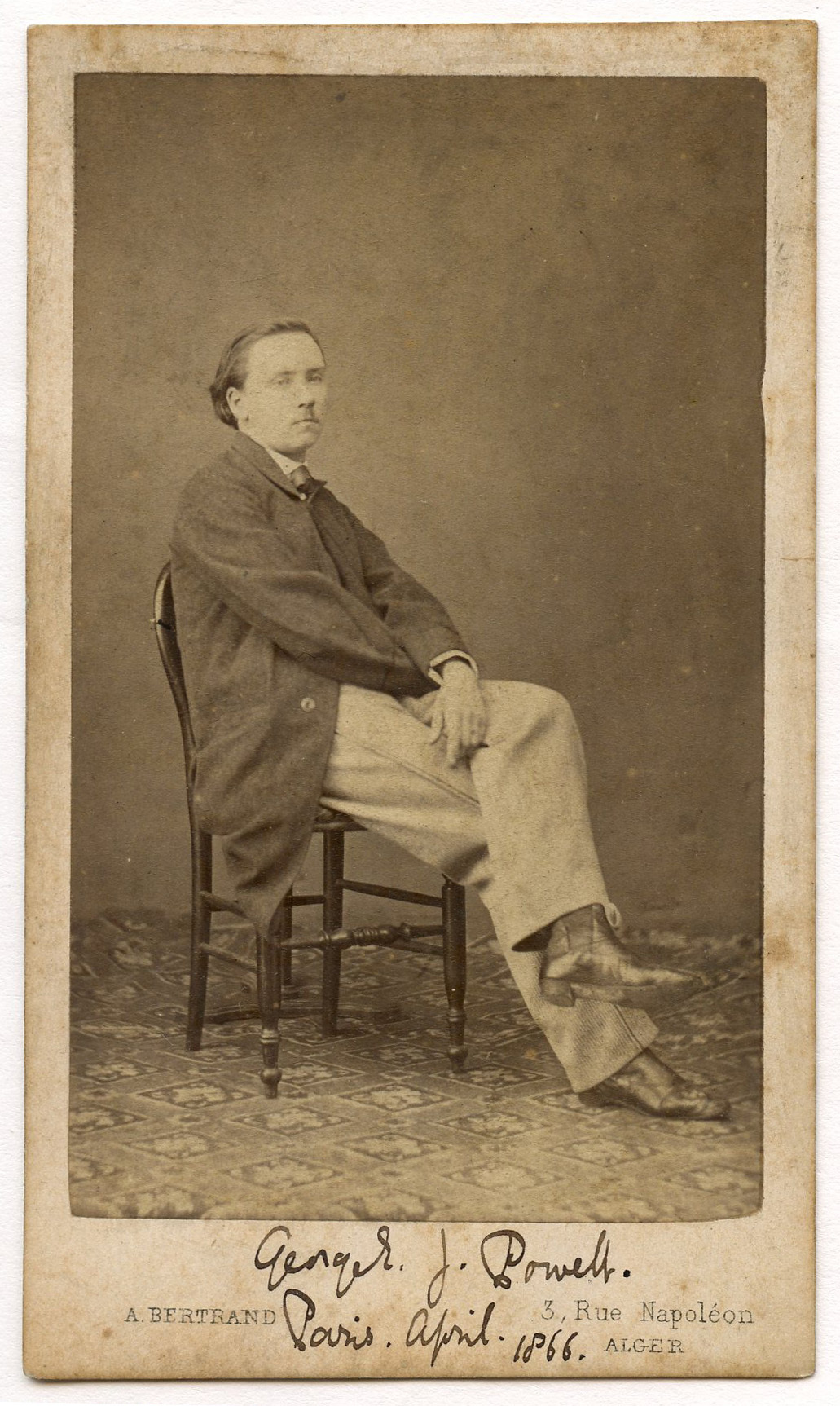 Full-length portrait of a white man. Man is seated at three-quarter view to his left. His legs are crossed. He wears a dark jacket and light pants. He has medium dark hair and a small mustache.