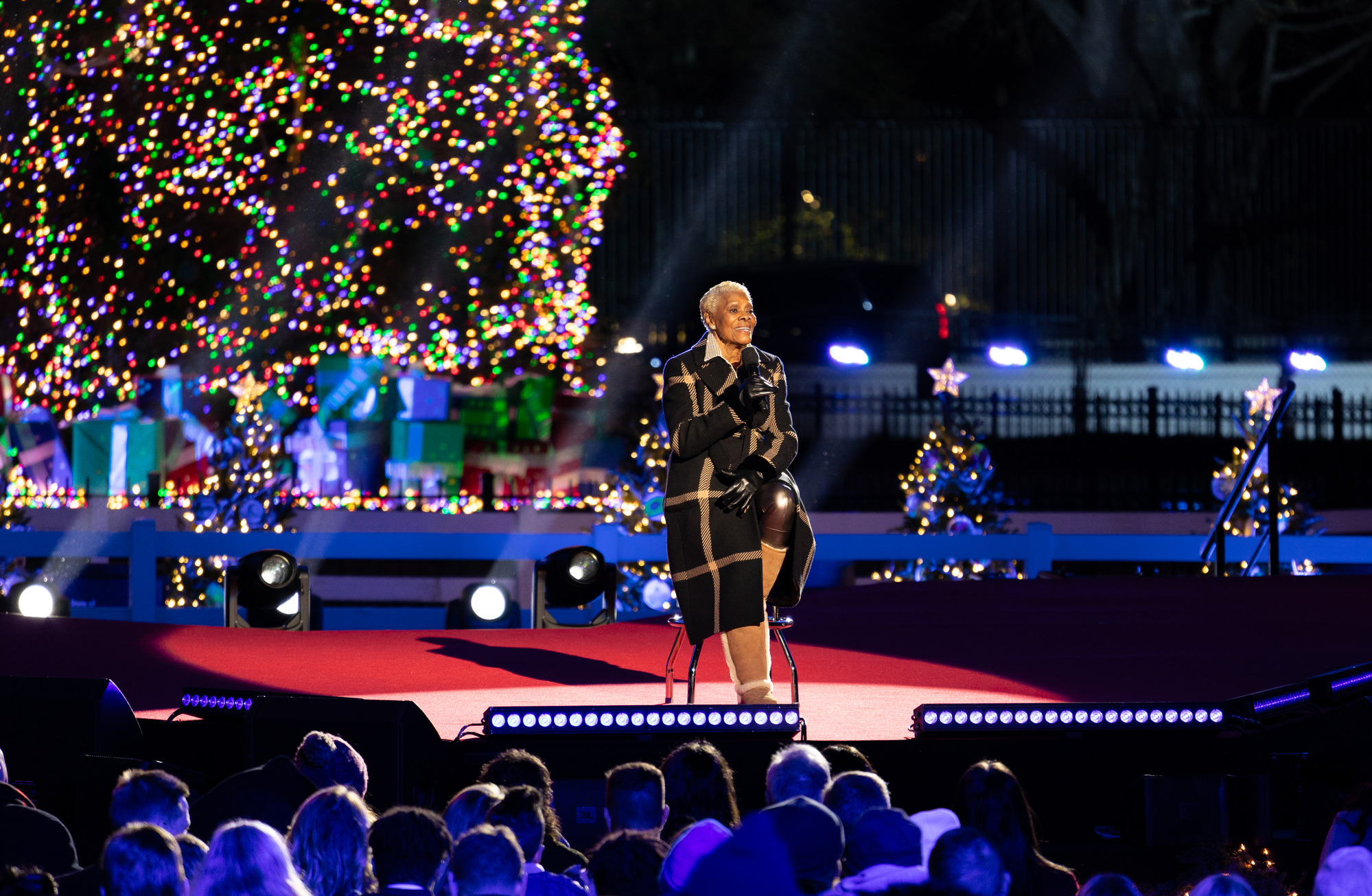 A women performs on a stage in front of a large Christmas tree
