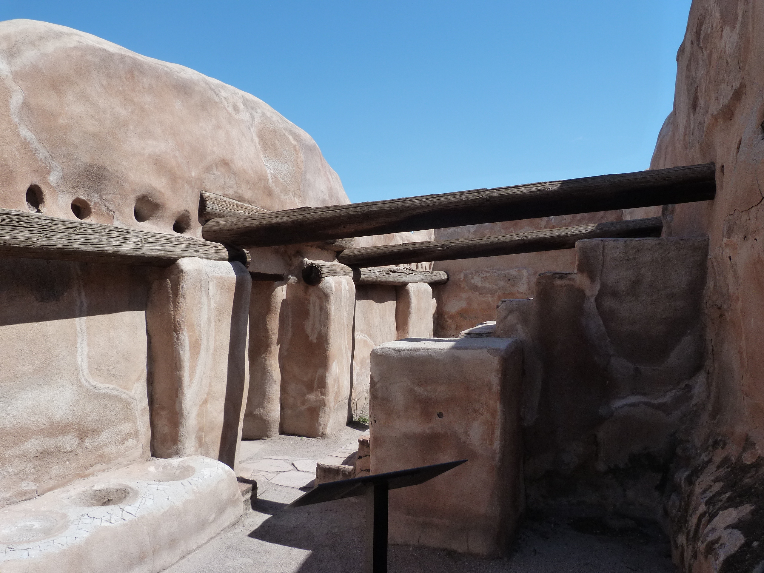 Storeroom with roof beams, stairway to the right, and low bench with pot divets to the left