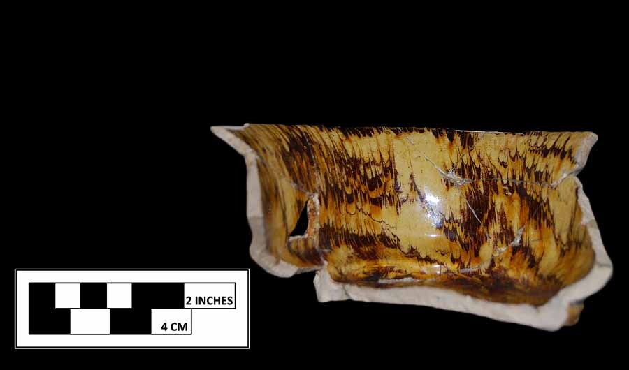 A broken staffordshire porringer, with a yellowish base and orangish brown mixture pattern 