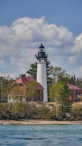 A white lighthouse surrounded by brick buildings rises out of Lake Superior