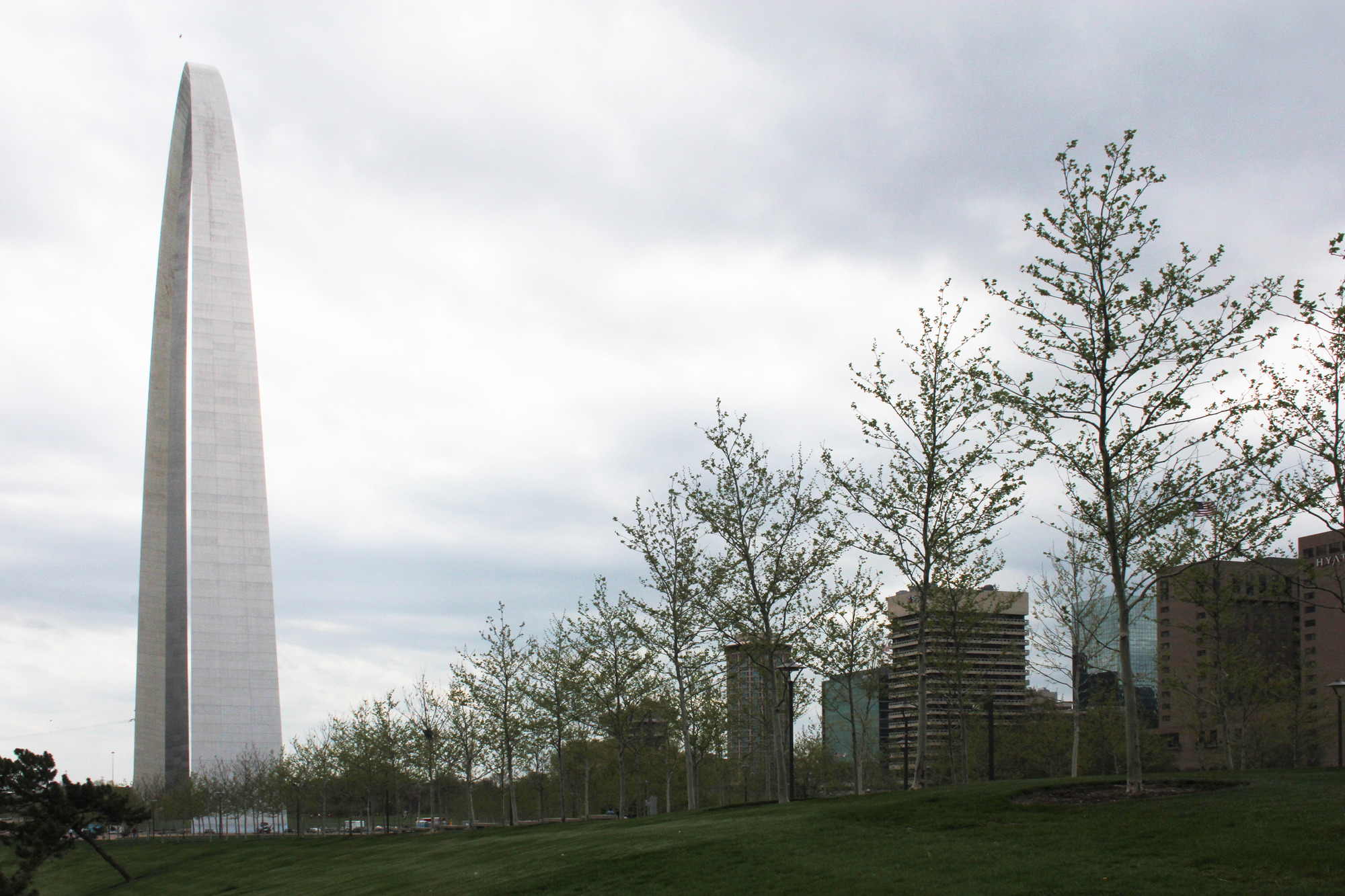 On the left Gateway Arch stands in front of a gray sky with trees and the St. Louis city scape off to the right.
