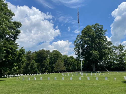 Uniform white grave markers are aligned in a curving row in an area of turf around a white flagstaff. 