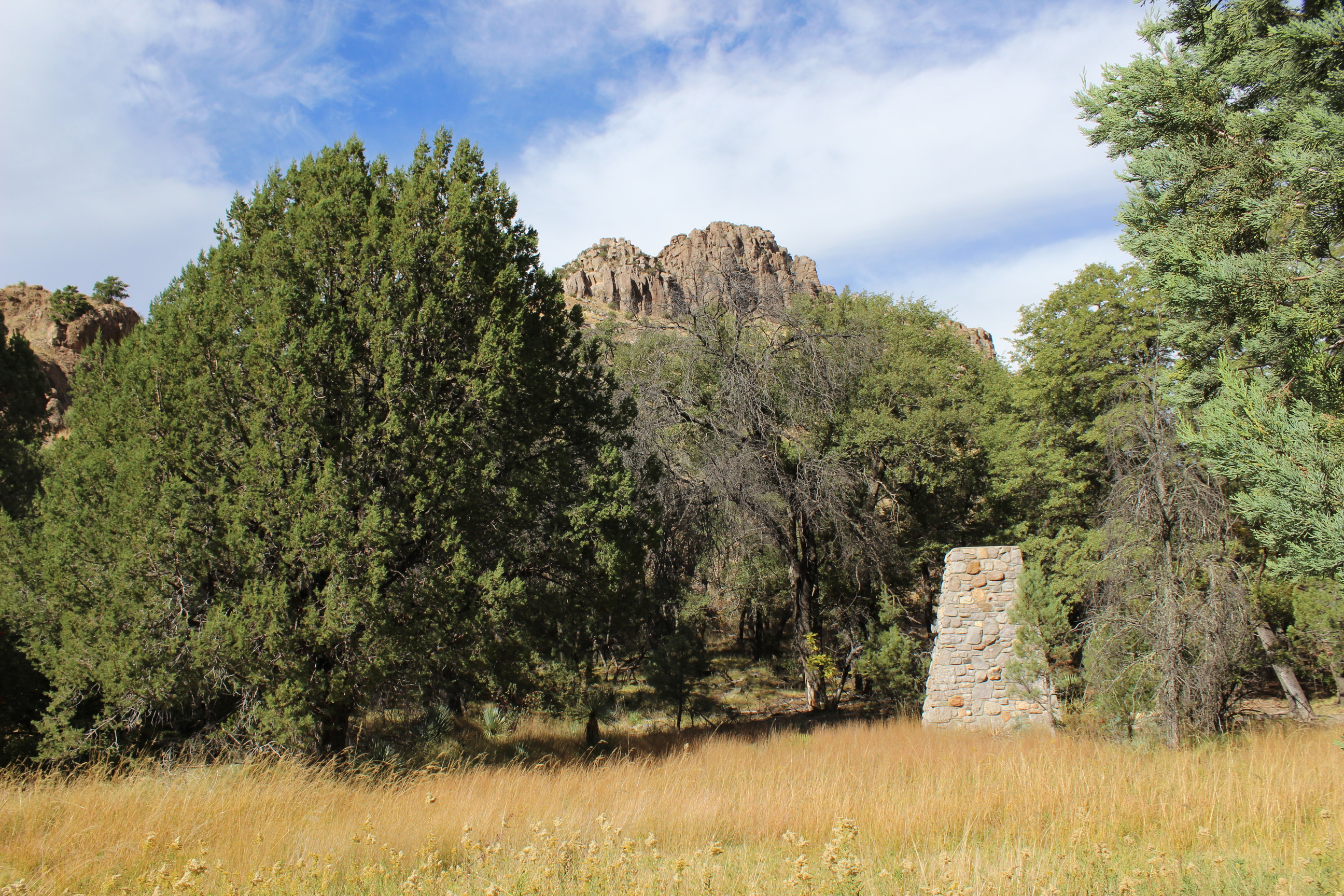 Stone chimney in a meadow with trees are rocky cliffs in the background. 