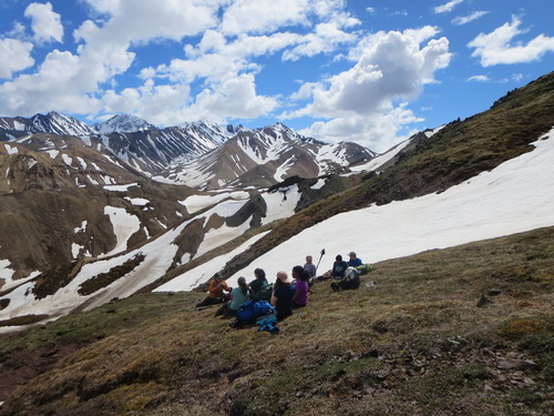 group of people sitting in a circle on a mountainside near a snow patch