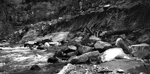 Stream erosion along highway, mud and rock bank along river fallen in.