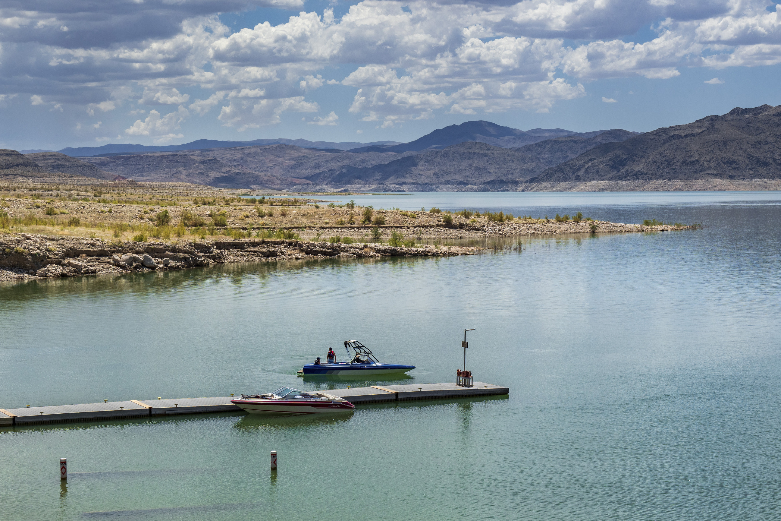 body of water surrounds boat dock with two boats,  cloudy sky and mountains in distance