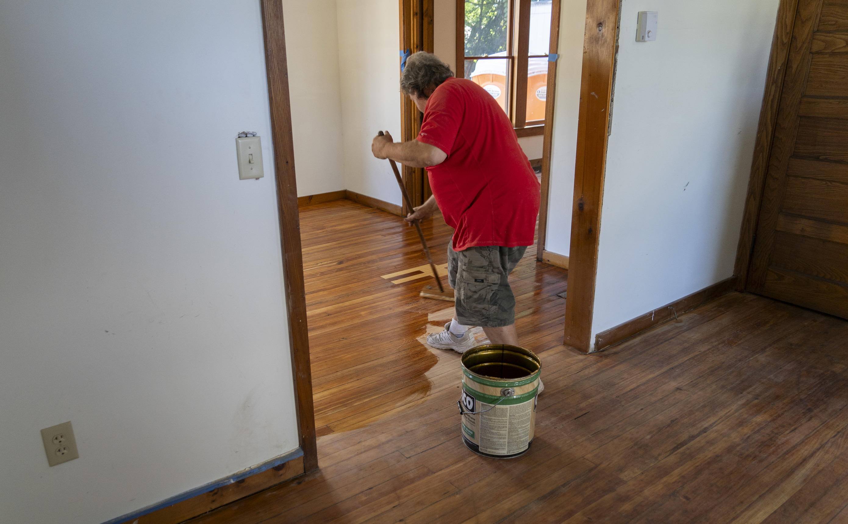 A man uses a mop to spread finish on the floors of a house.
