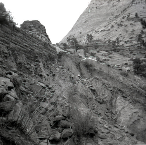 Men standing next to retaining wall in need of repair along East Rim road, trucks parked up on road.