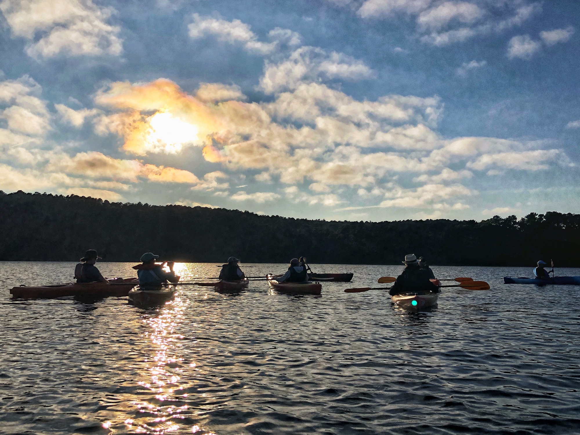 Six people in kayaks view the setting sun.