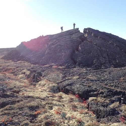 Photograph of two people hiking on a large volcanic feature. 