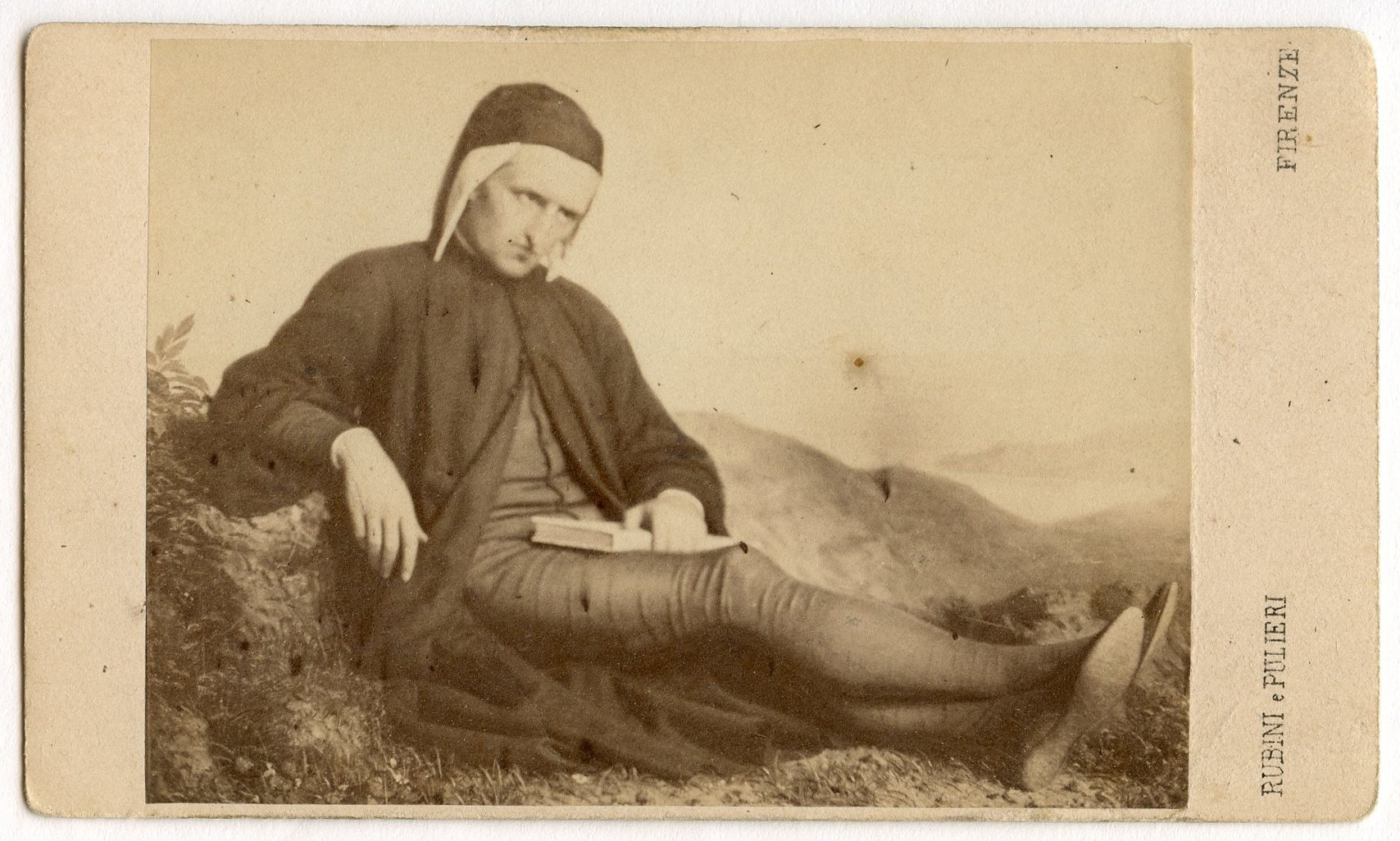Painting of Dante sitting on the ground with a book open in his left hand. Mountains are in the background.