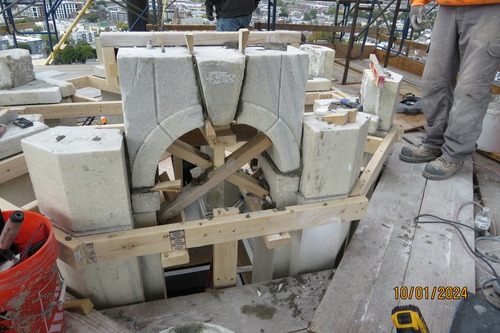 Wood frames holding up marble blocks being placed together to form an arch. workers stand on scaffolding that surrounds the top section of the arch. 