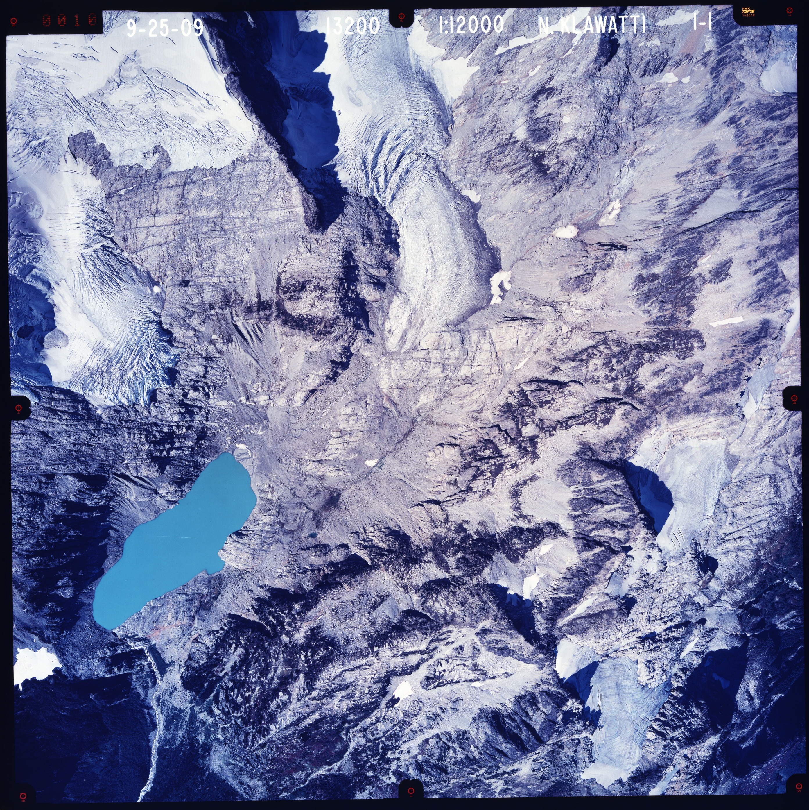 Color aerial photograph of glacier, snowfields and alpine lake on mountain peak.
