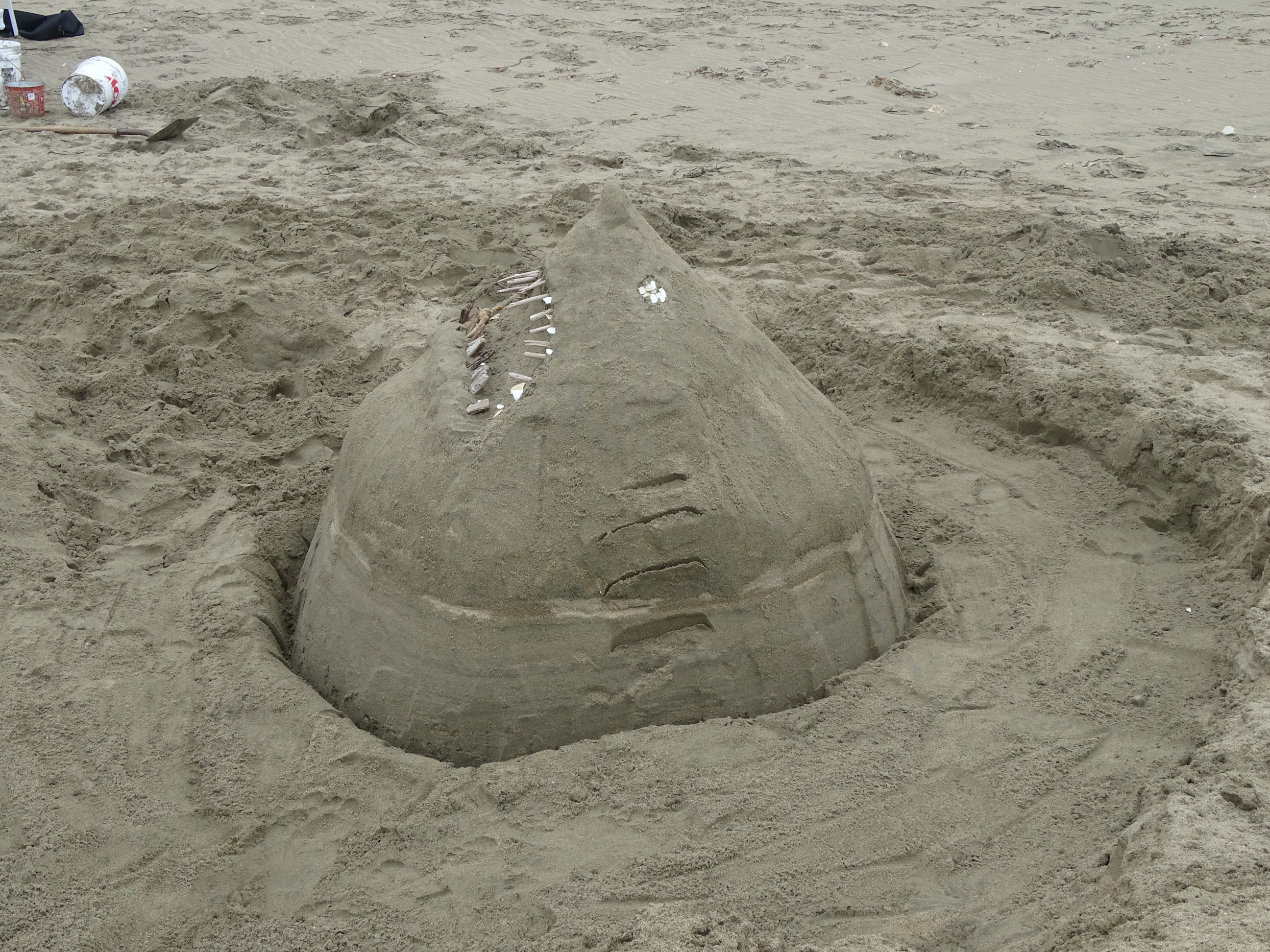 A sand sculpture of a shark's head rising out of the sand.