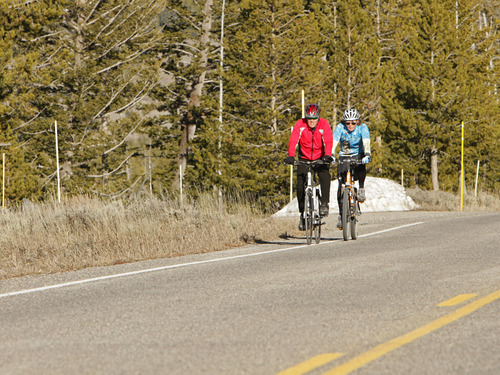 A man and a woman bicycling on the side of the road. 