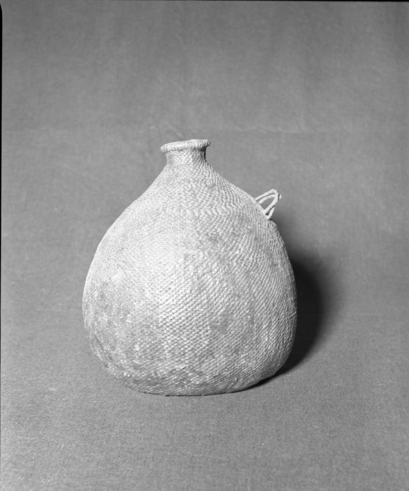Mrs. Donald Segerstrom Collection. Object: Paiute water jug. Dimensions: 11" height. Materials: all willow, pitch. Technology: start in three strand twining, body in diagonal twining, band of plain twining over paired warps at shoulder, commercial leather loops. Collection History: ---. Photographed of Michael Dixon, 1/83. Catalogued by Craig Bates and Barbara Beroza. Yosemite Collections, National Park Service.