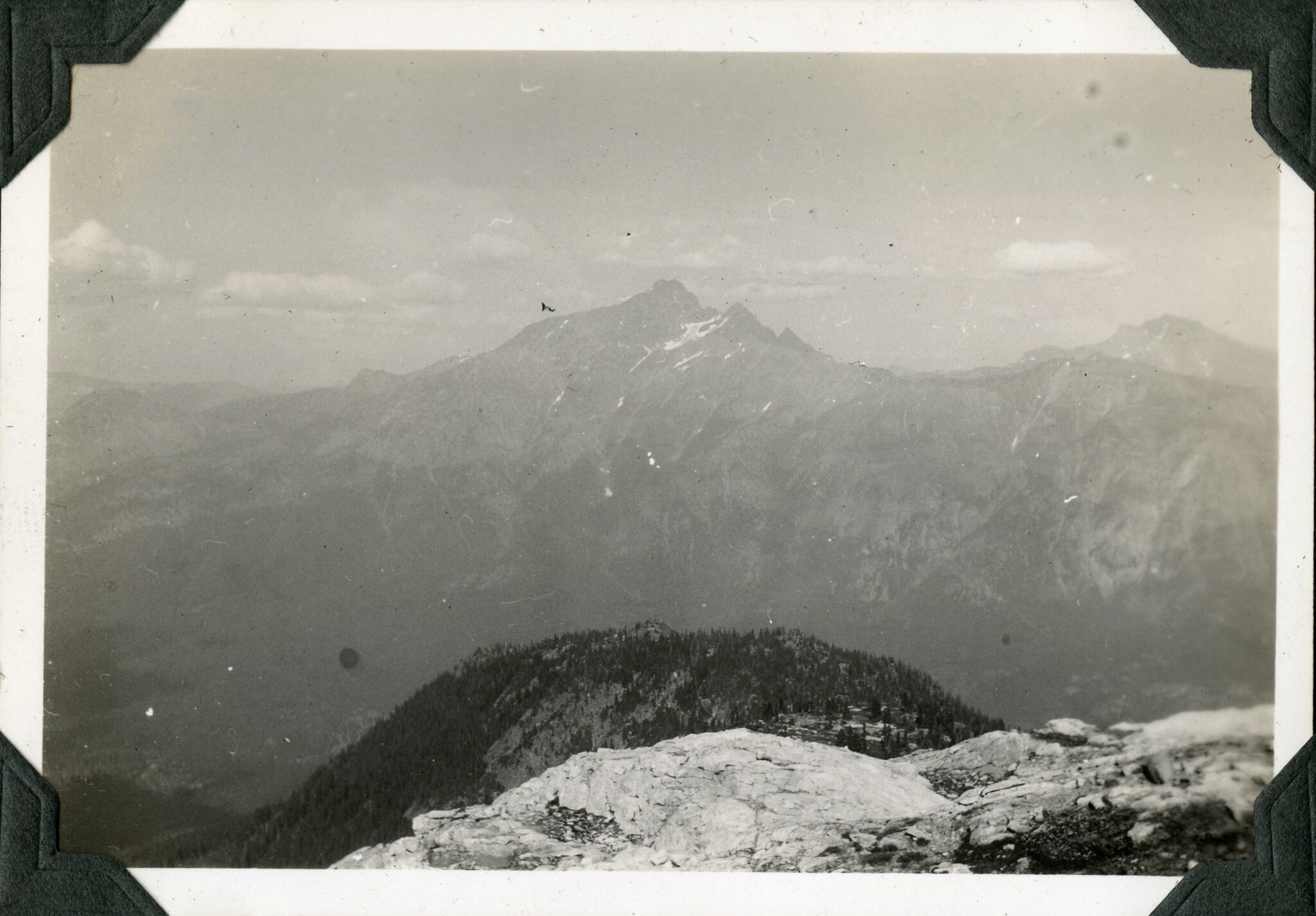 A distant view of a mountain with fluffy clouds and a cliff ledge in the foreground.