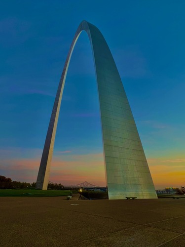 Orange, pink, and yellow sunrise reflects onto the legs on the Gateway Arch.