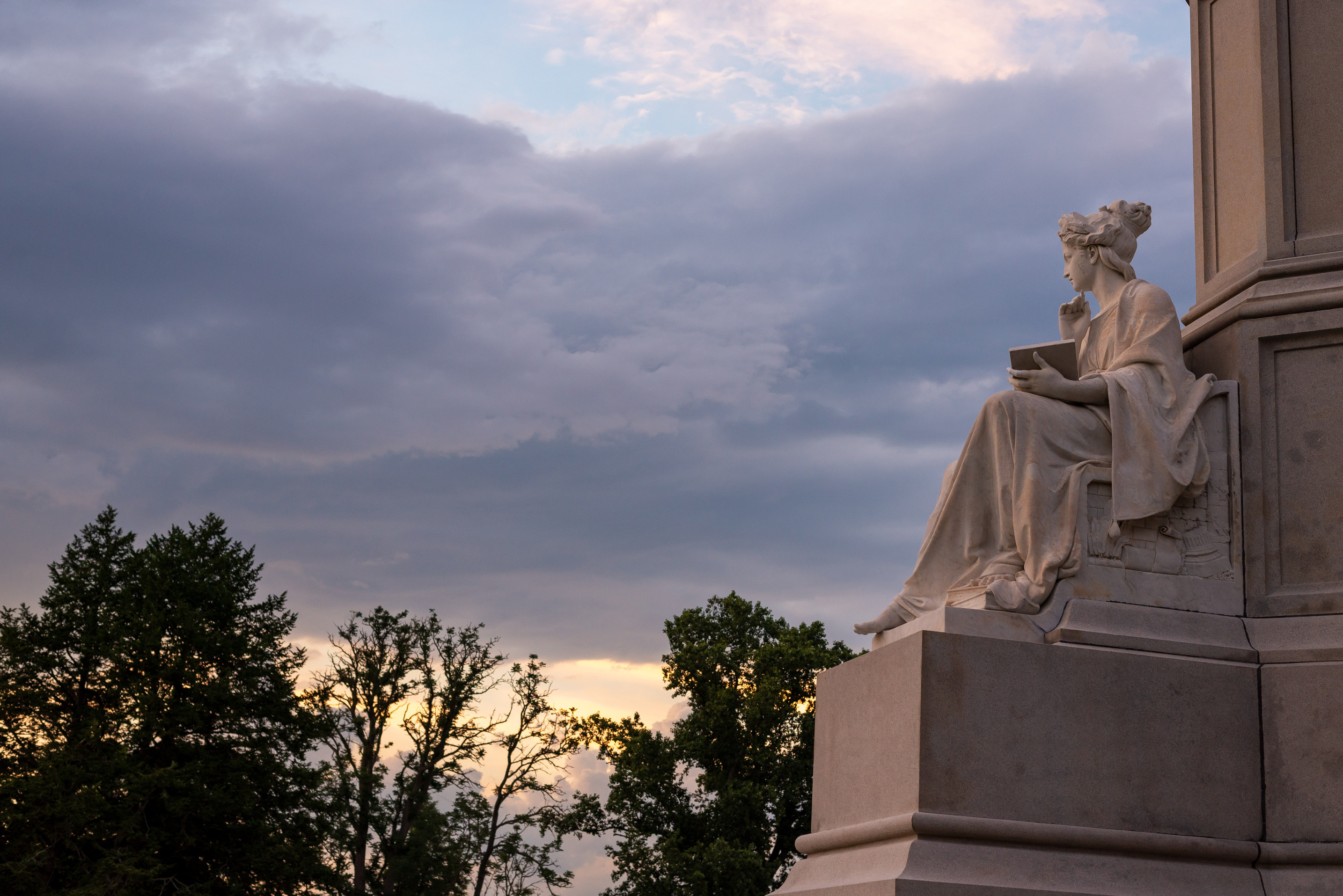 A granite statue of a robed lady holding a tablet.