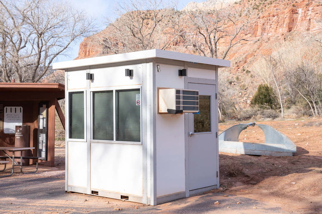 Small square temporary building with fields and sandstone cliffs in the background