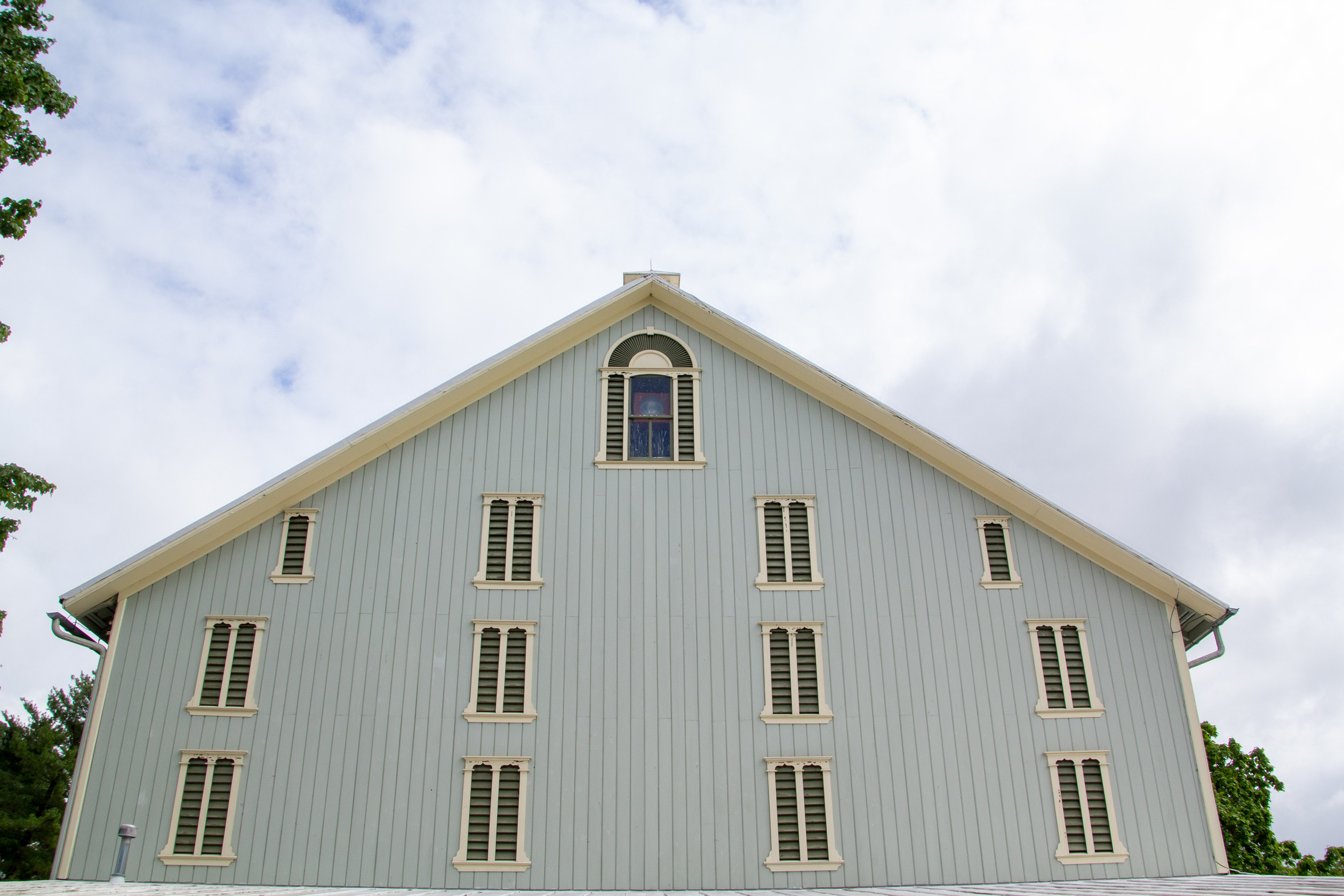 A side of a blue painted barn with a window at the top with a floodlight in it.
