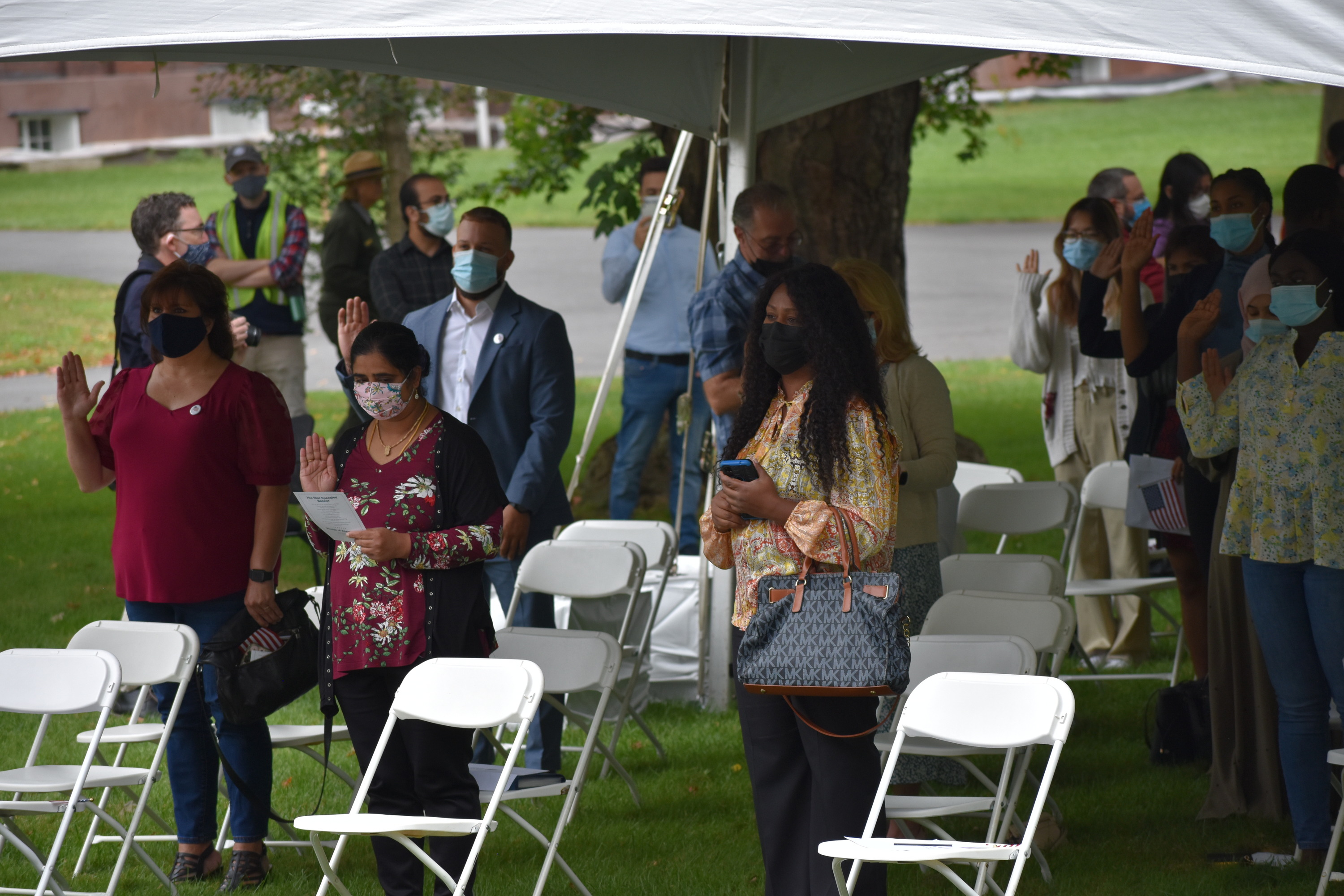People stand underneath a tent with their right hand raised taking an oath. 
