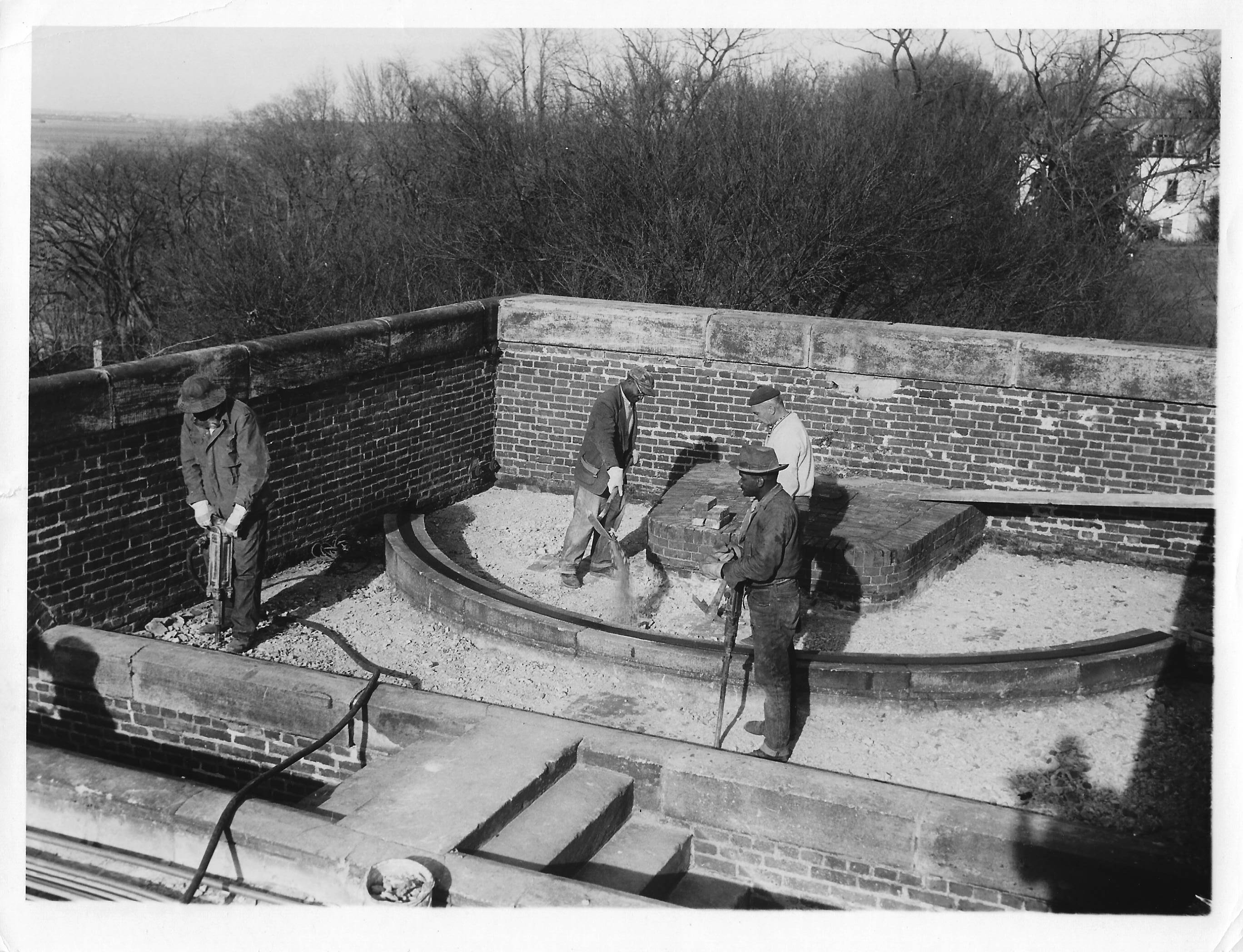 Four workmen, two with jackhammers the other two have picks.  The are removing the concrete from the brickwork.  