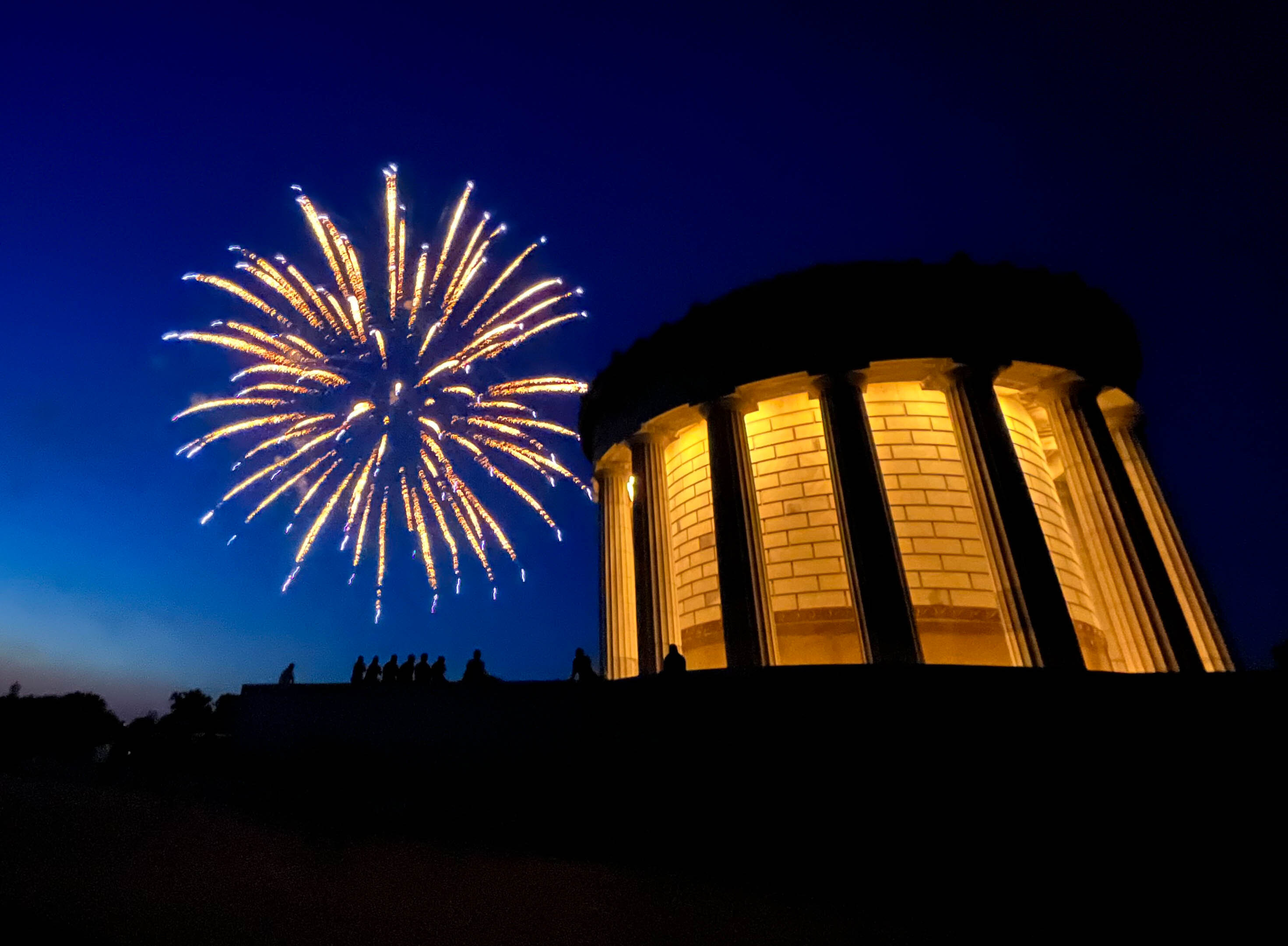 Nighttime fireworks over circular memorial building with prominent columns