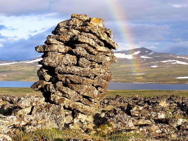 Stone structure with a rainbow over a lake or river in the background 