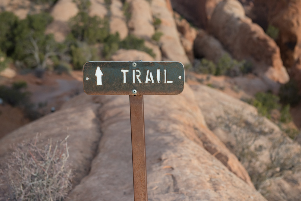 a brown metal sign with a white arrow and text that says "trail"