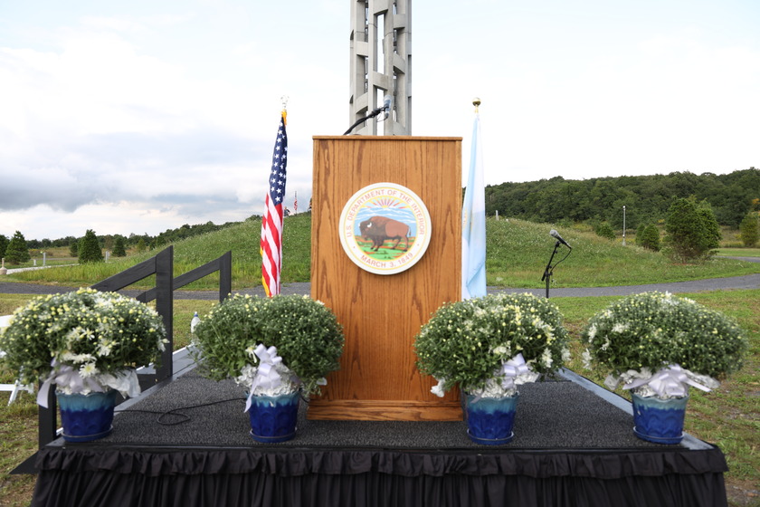 Stage at the base of Tower of Voices with a podium, two flags, and flowers.