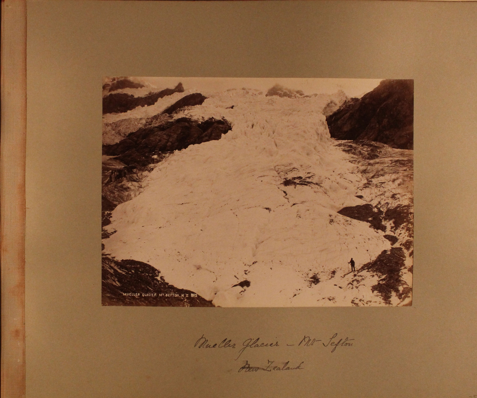 View of massive expanse of  snow moving through craggy mountains. Solitary mountaineer at lower right corner.