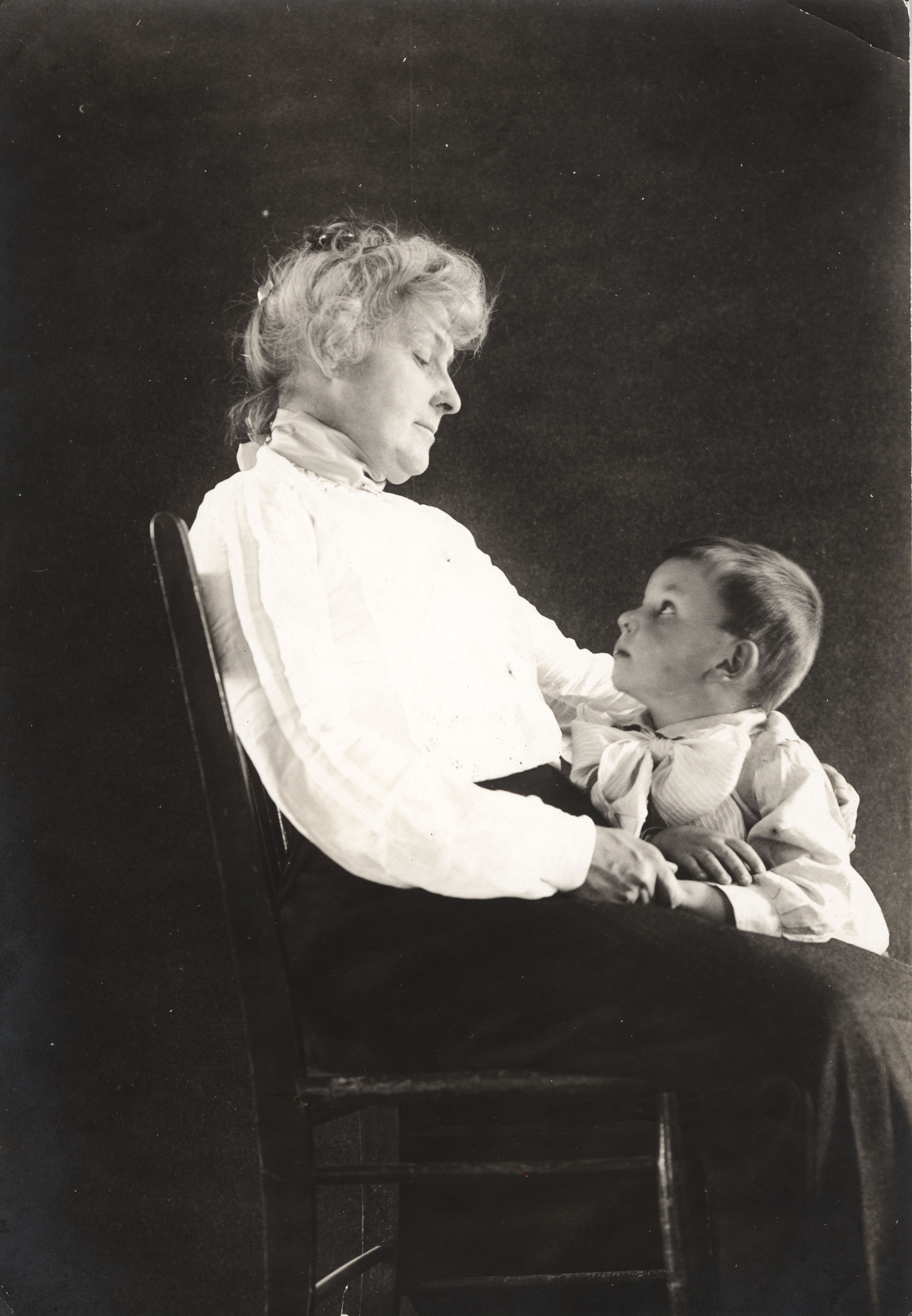 Black and white photograph of a woman seated in a chair with a young boy looking up at her