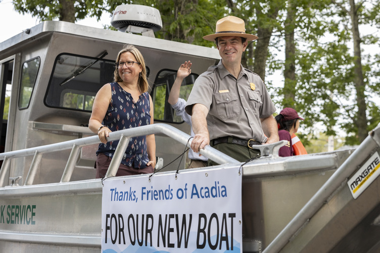 Superintendent Kevin Schneider and his wife stand on a new boat with a banner reading "Thanks, Friends of Acadia FOR OUR NEW BOAT."