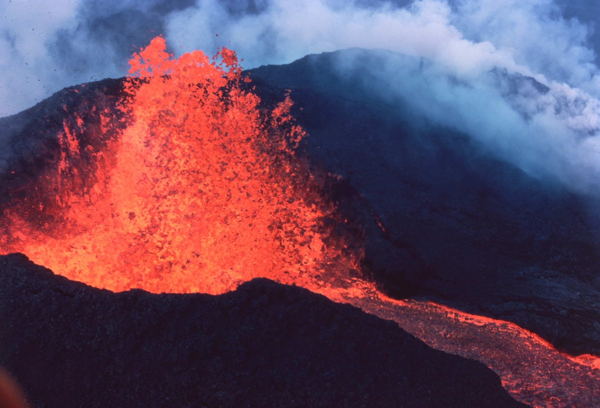 Glowing lava fountain with blue plumes of steam beyond