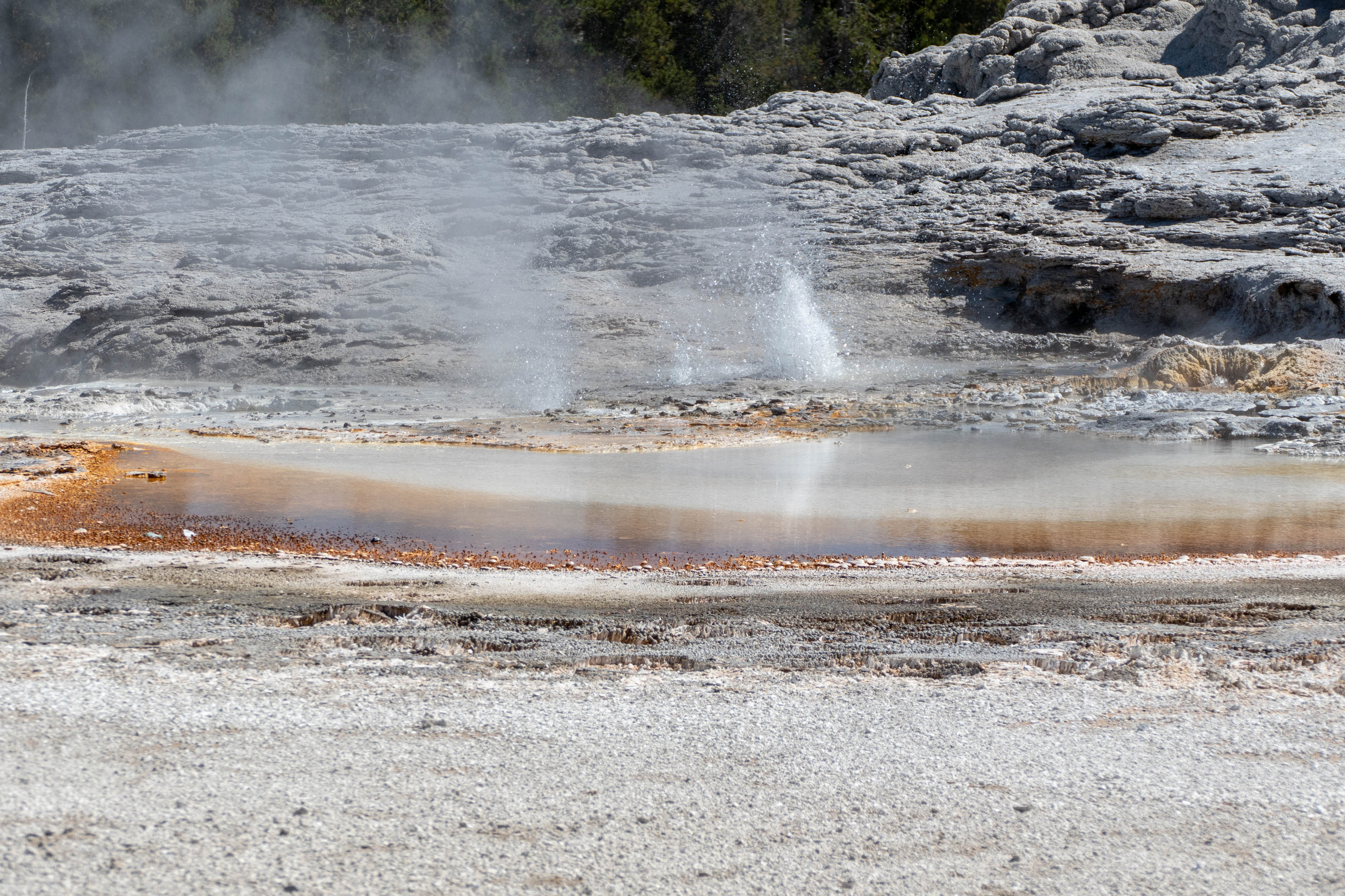 Small eruption if taking place in front of a large geyser cone