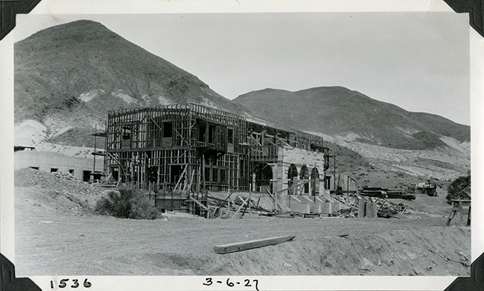This is an historic black and white photograph from the Scotty's Castle Historic Photograph Collection, Death Valley National Park of Scotty's Castle Main House, looking northeast. Wood framing in preparation for installing hollow tile walls. Great Hall roof pearlings in place. Lower Music Room windows installed. Solarium foundation formed at left. March 6, 1927. Photographed by Mat Roy Thompson.