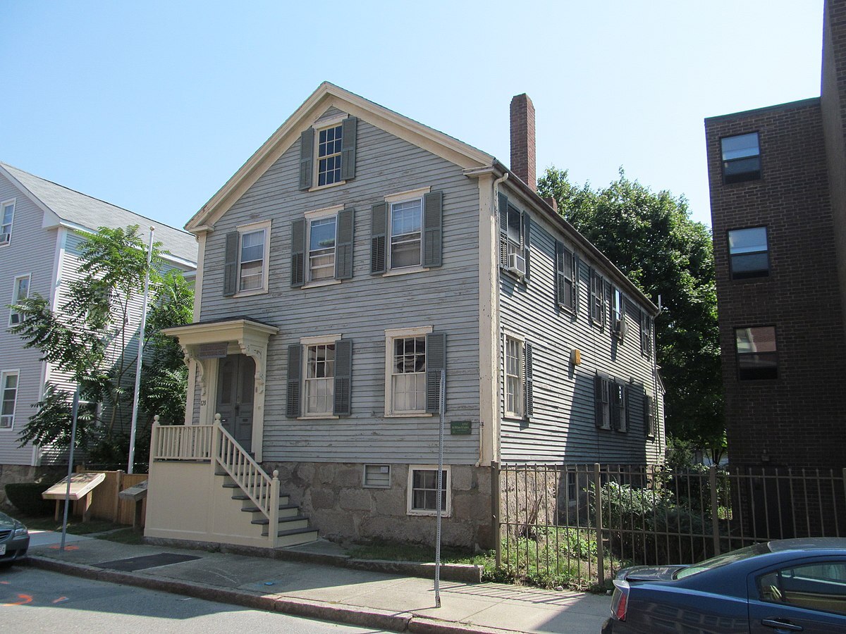 Photograph of wooden house with a small staircase leading to the front door, and multiple windows on the front and side.