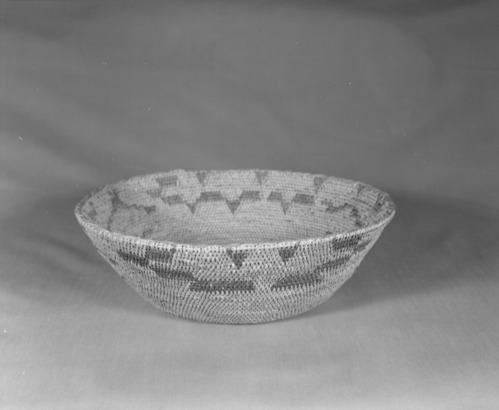 Private Collection. Object: Miwok basket. Dimensions: 12 x 3-3/4". Materials: Redbud, bracken fern, & bull pine. Technology: Single rod, fag ends trimmed on work face, moving ends trimmed on interior. Leftward coil direction. Rim overstitched three times through top rod with two back stitches at coil ending. Overstitched large clockspring start. Triangular design unit group in redbud, linear design units in bracken fern root. Collection History: Made by Matilda, 1920s. Photographed by Michael Dixon. Catalogued by Craig Bates and Barbara Beroza. Yosemite Collections, National Park Service.