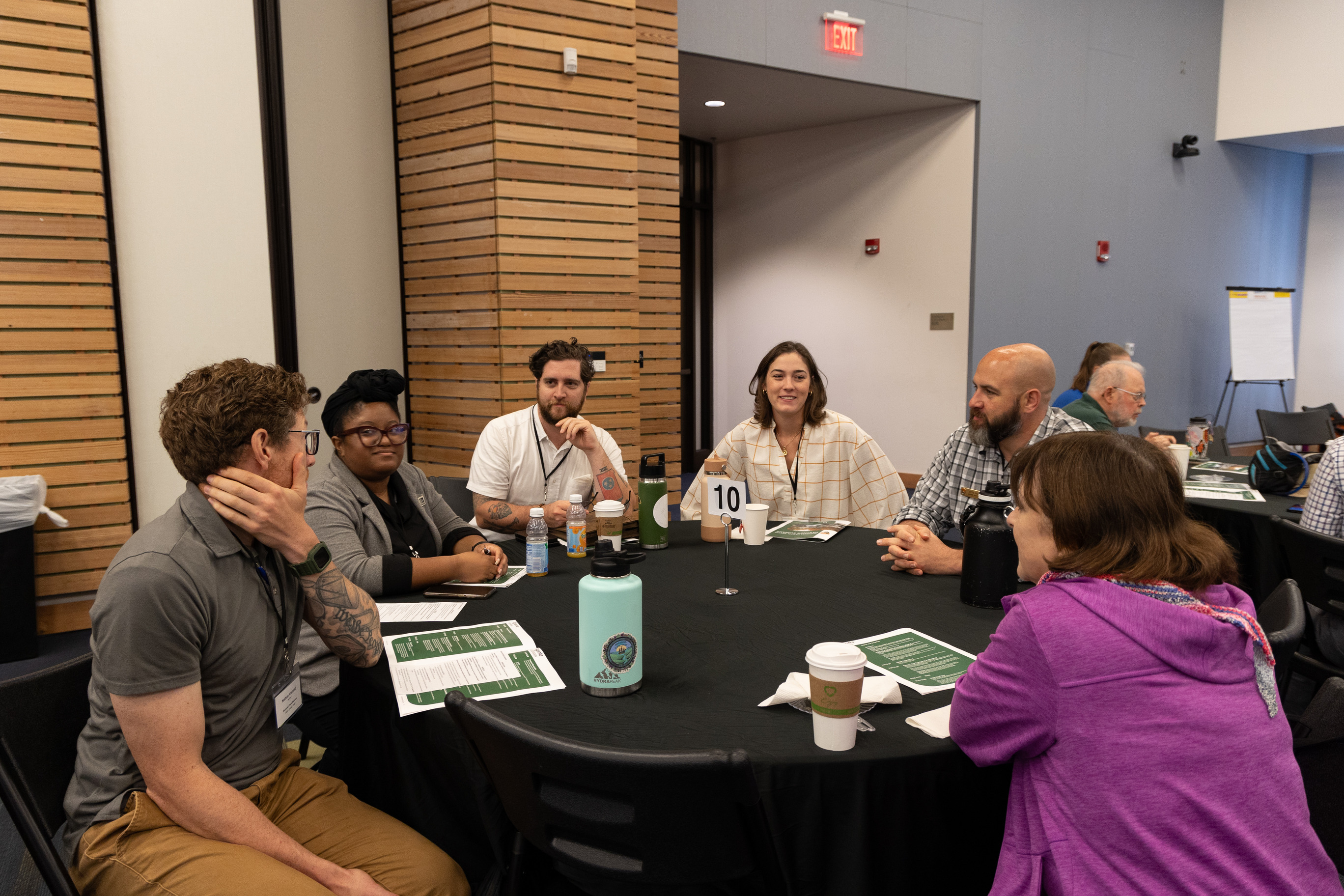 A group of six people sit around a circular table. 