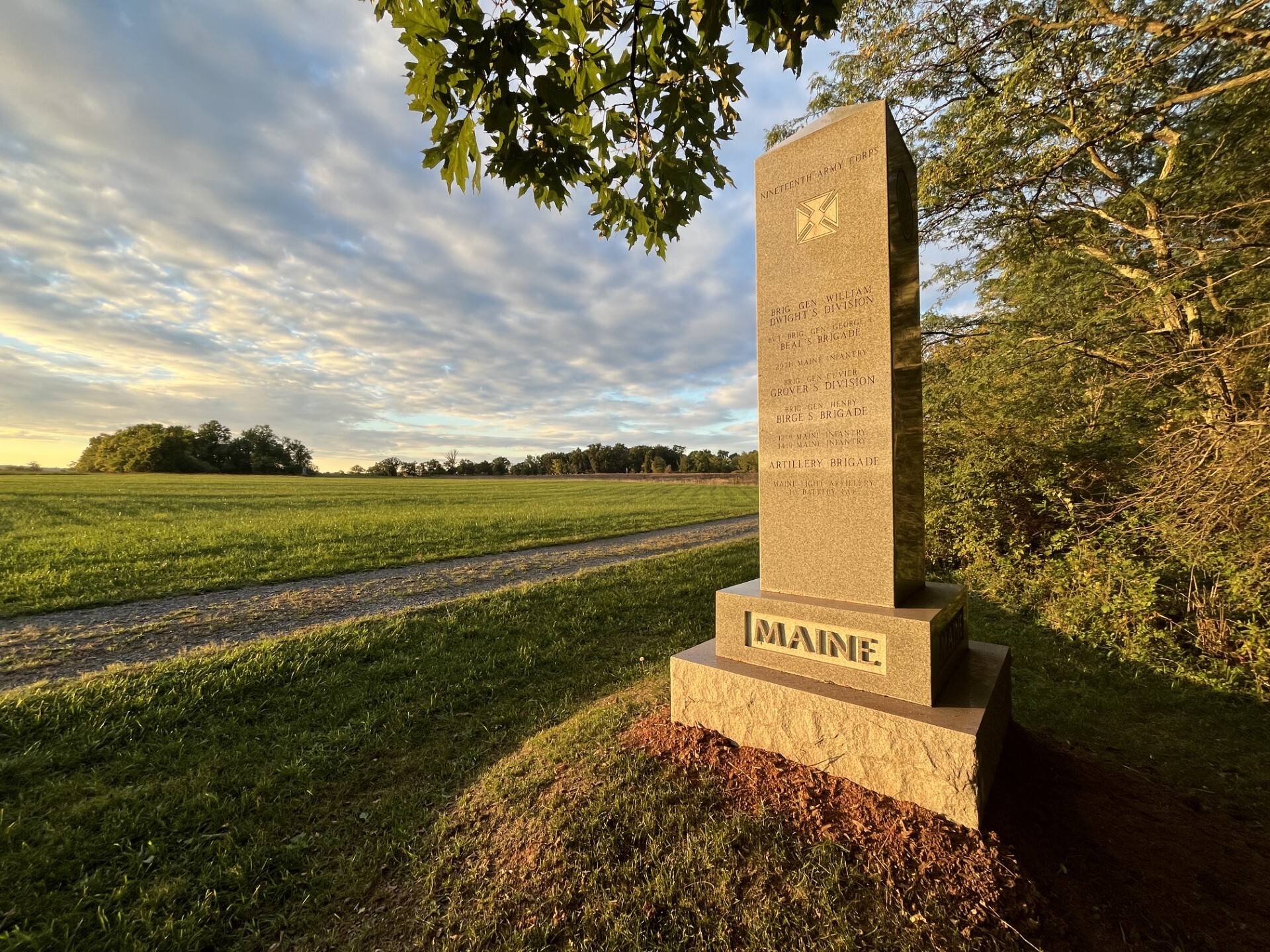 A vertical monument inscribed "Maine" next to a large open grassy field. 