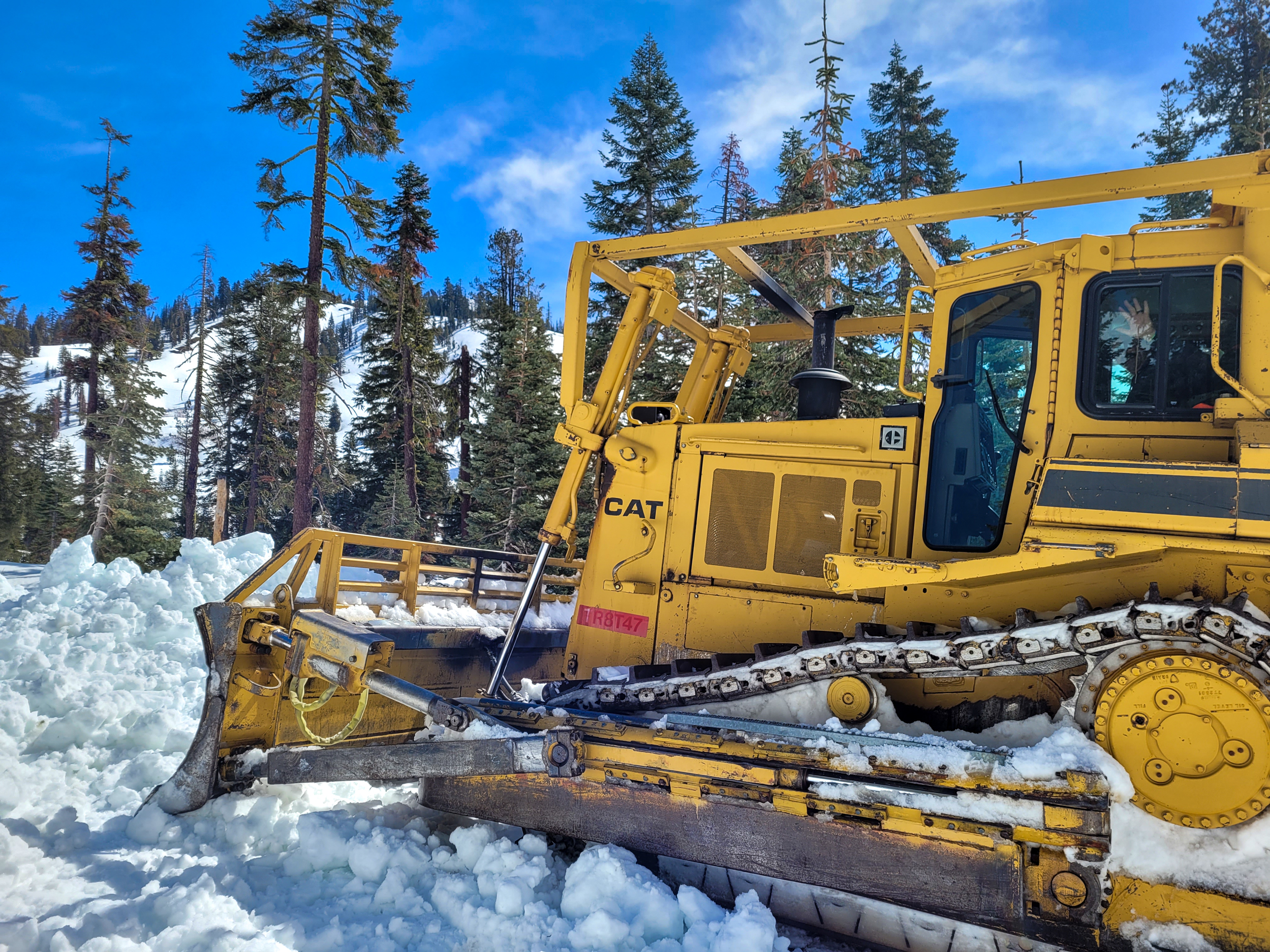 A yellow bulldozer sits on the side of a snow-covered road.
