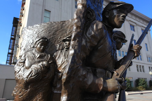 A curved bronze statue with African American Civil War soldiers on the front side and the family of a soldier on the backside. 