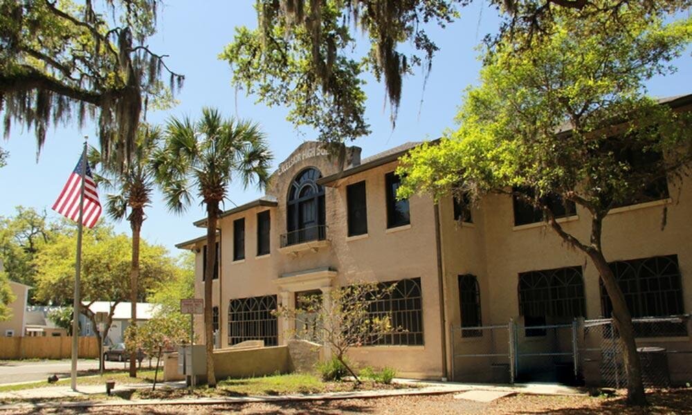 A large two-story tan stucco building surrounded by trees.