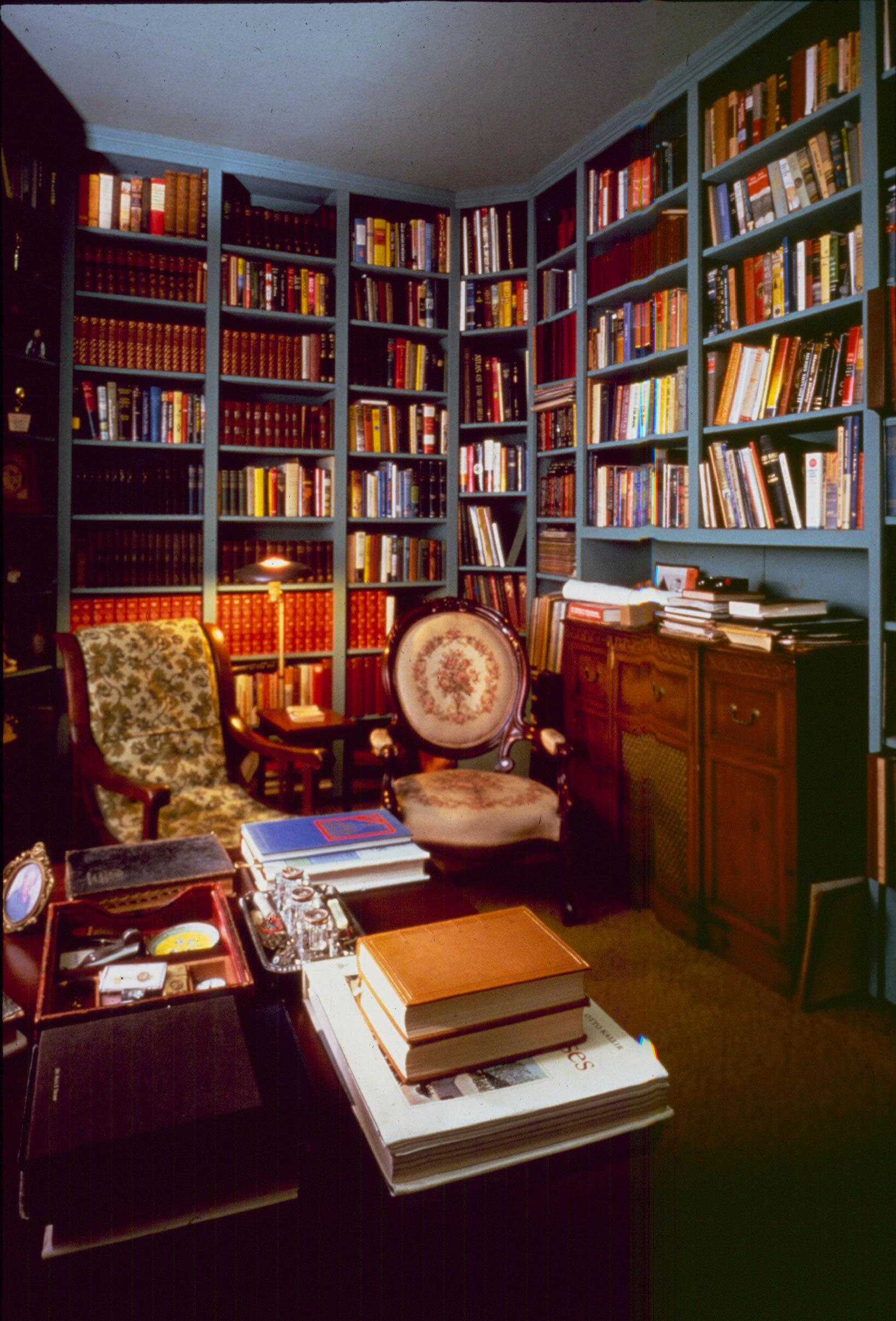 The study. Dozens of shelves are filled with books and records. Two chairs in this photograph. A radio console is prominent.