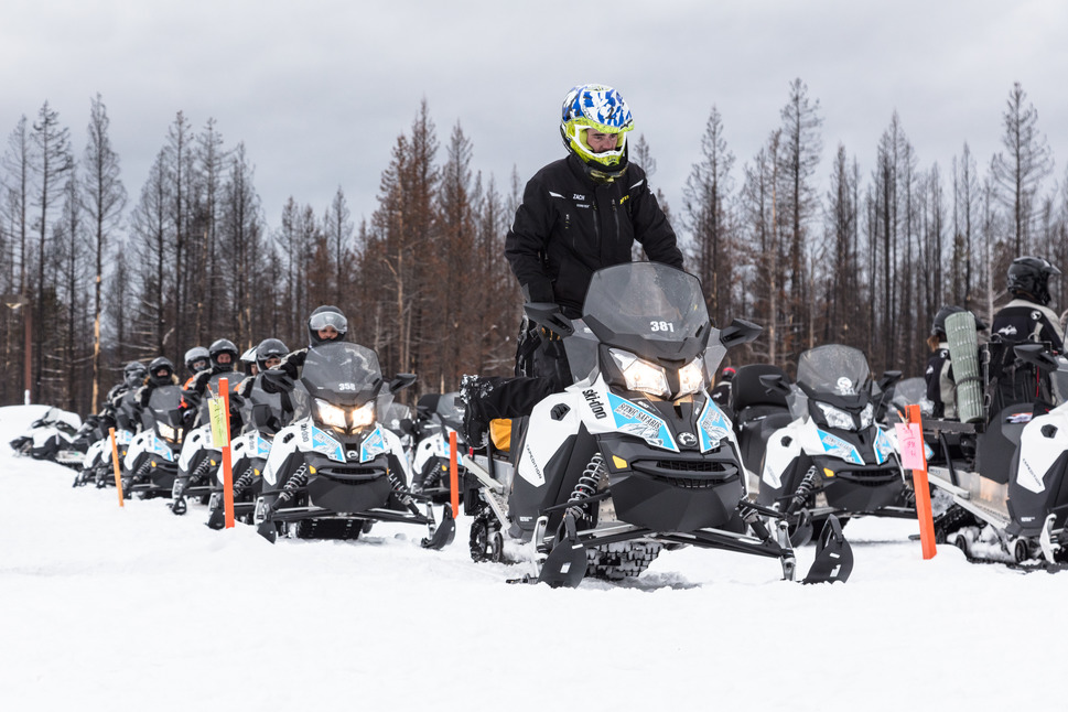 A line of snowmobilers getting ready to pull out of parking lot